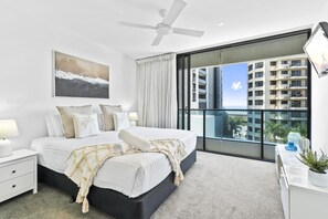 A modern bedroom with a large bed, a ceiling fan, a view of the city, and a balcony with a railing. - Cozy 1 Bedroom + Study Unit in Broadbeach - Q Stay (Broadbeach)
