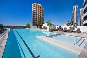 A swimming pool with lounge chairs and a view of tall buildings. - Cozy 1 Bedroom + Study Unit in Broadbeach - Q Stay (Broadbeach)