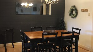 Ein Esszimmer mit Holztisch und -stühlen, einer Chandelüster, einem Spiegel und einem Kranz an der Wand.