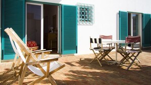 Eine Außenpatio mit einem Holztisch und Stühlen, einem kleinen weißen Tisch und einer blauen Tür mit Fensterläden.
