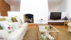 Ein Wohnzimmer mit einem weißen Sofa, einem Glastisch, einem Kamin, einem Fernseher und einem TV-Schrank.