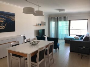 Una sala de estar moderna con comedor, televisor de pantalla plana y un ventanal con cortinas.