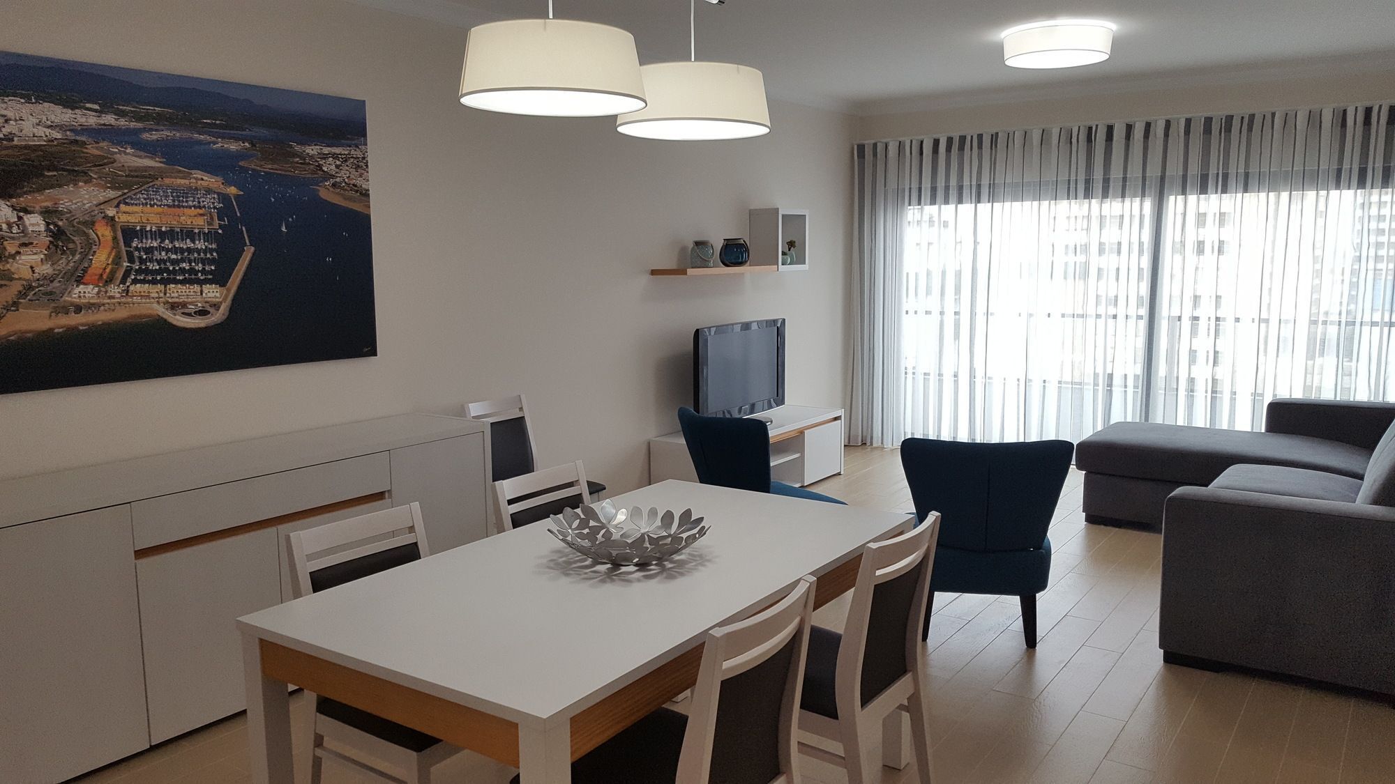 A modern living room with a dining area, a TV, and a large window with curtains.