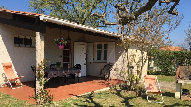 Una casa con un porche cubierto, una mesa con sillas y una maceta colgante.