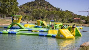 Parque acuático al aire libre con estructuras inflables y un lago al fondo.