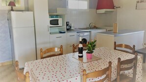 Cocina compacta con microondas, lavamanos y una pequeña zona de comedor con mesa y sillas.