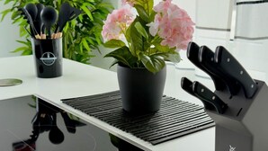 Une cuisine moderne dotée d’une plaque de cuisson à induction noire, d’un bloc à couteaux et d’une plante en pot aux fleurs roses.