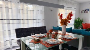 Un coin repas avec une table en verre, des chaises et un vase rempli de feuilles d’automne.
