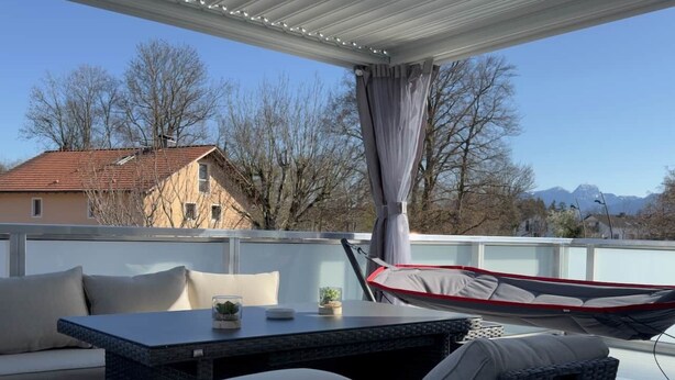 Une terrasse extérieure avec des meubles en osier, une table avec des coussins et un hamac.