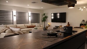 A modern kitchen with a marble countertop, a dining area with a sofa, and a TV mounted on the wall. - Modern Waterfront home w/ Game Room & Private Dock (Cape Coral)