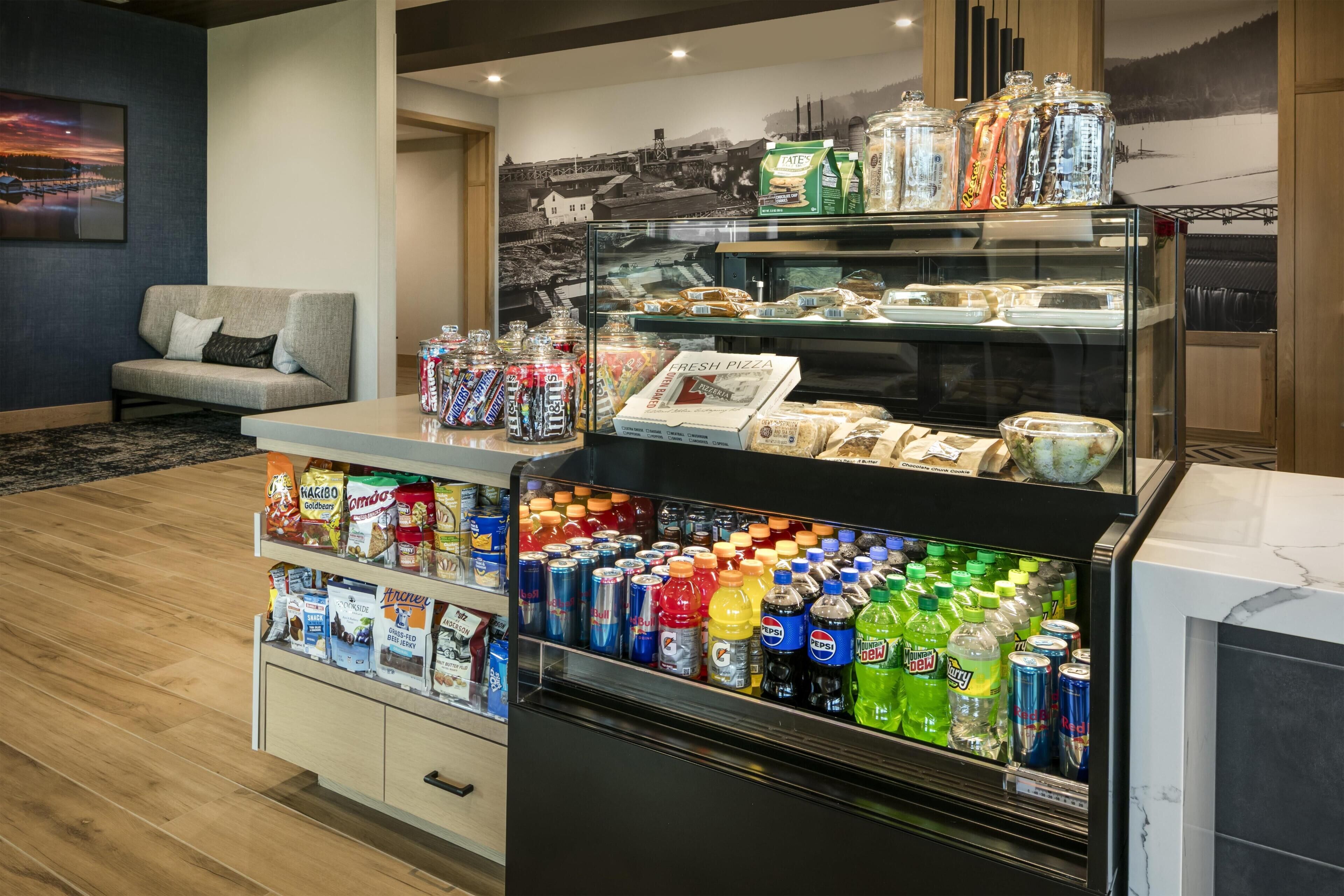 A hotel lobby with a snack bar featuring a variety of snacks, beverages, and a fresh pizza display.