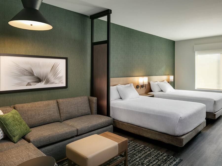Una habitación de hotel con sofá, dos camas, una obra de arte enmarco y una ventana.