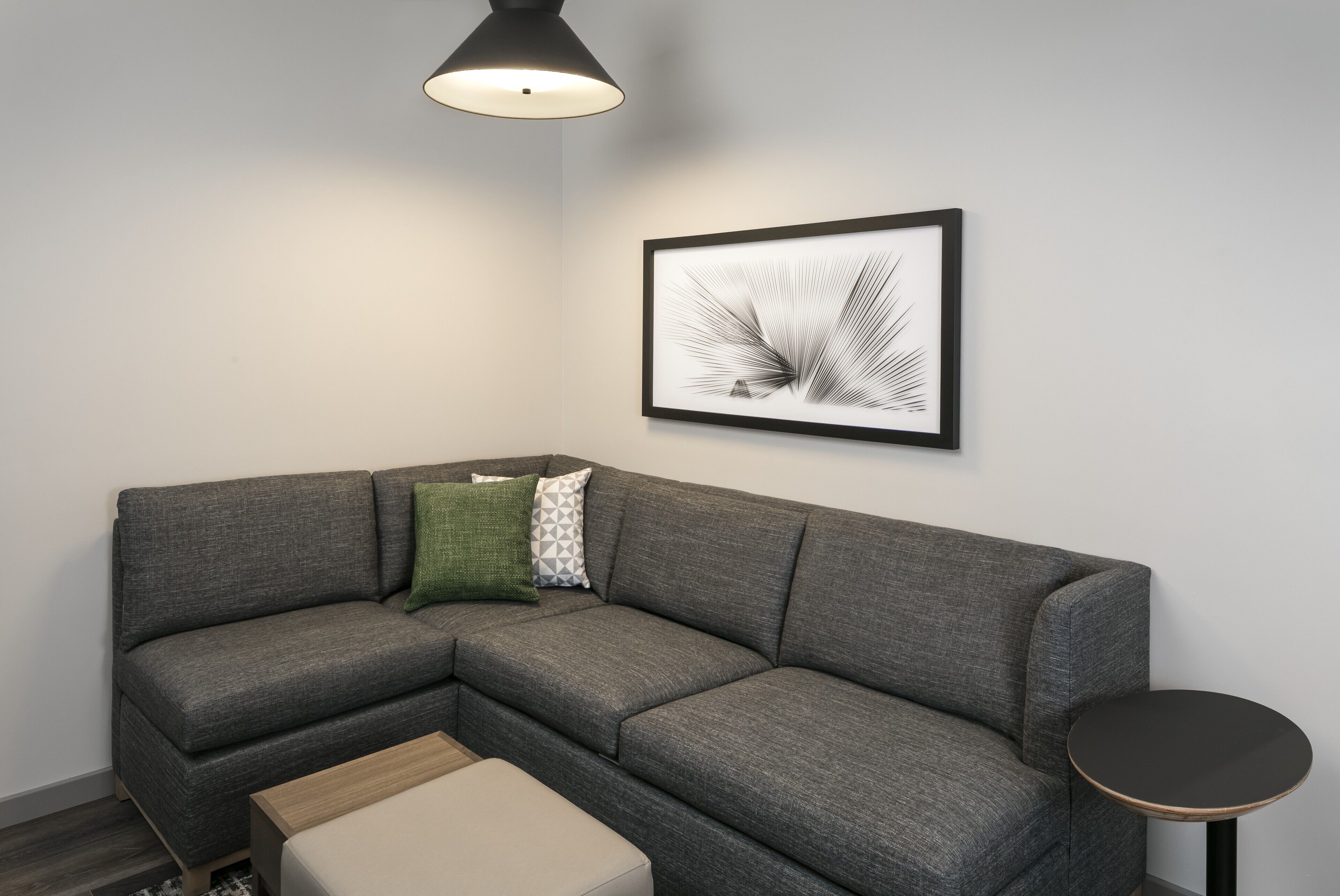 A modern living room with a grey sectional sofa, a small round table, and a framed abstract artwork on the wall.