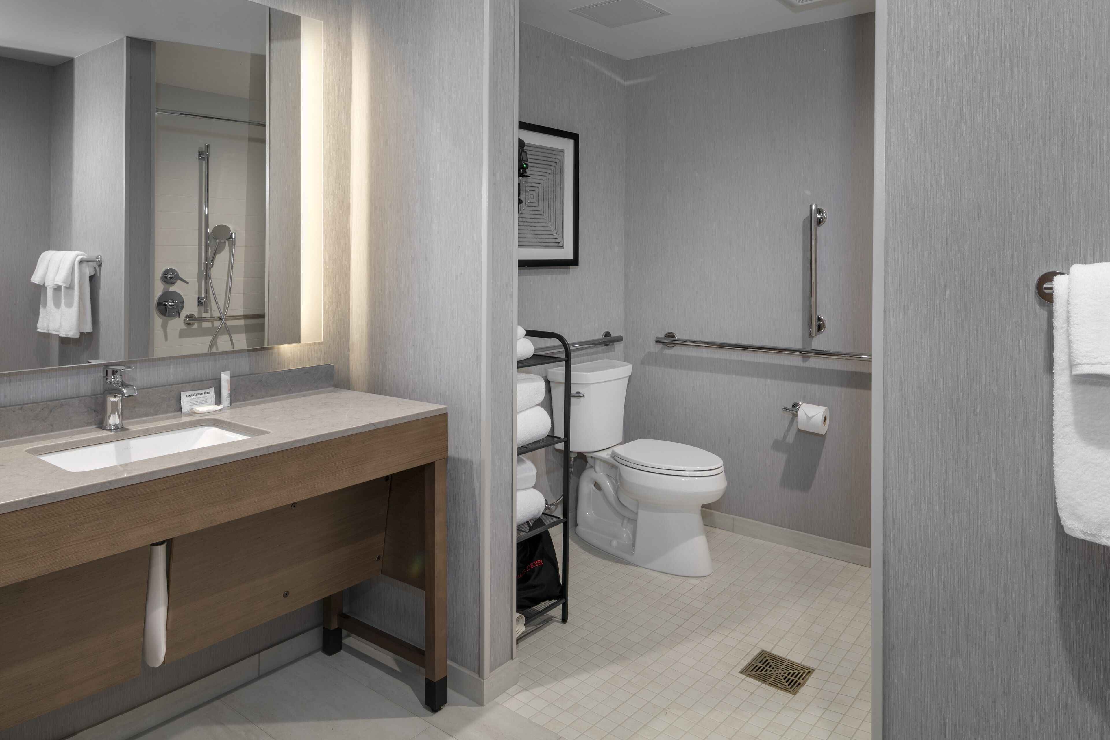 A modern bathroom with a dual sink vanity, a toilet, a shower, and a grab bar.