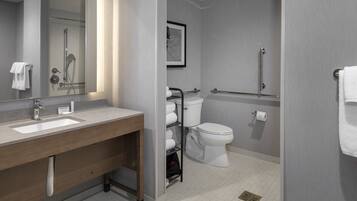 Un baño moderno con tocador de doble lavabo, inodoro, ducha y barra de apoyo.