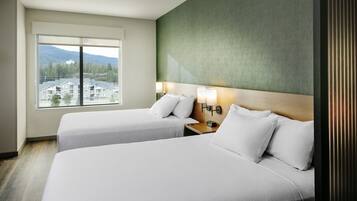 A hotel room with two beds, a large window with a view of buildings and mountains, and a green accent wall.