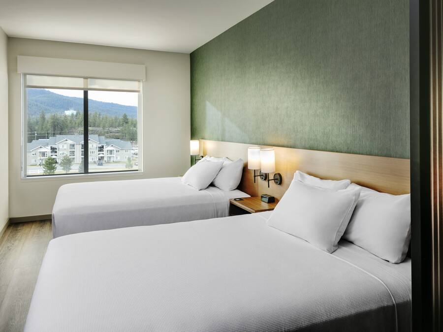 A hotel room with two beds, a large window with a view of buildings and mountains, and a green accent wall.