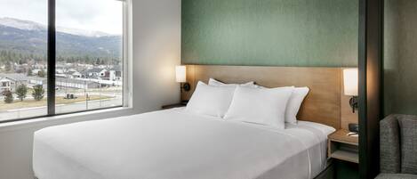 Habitación de hotel con una cama grande, vistas a un pueblo y montañas, y una pared verde decorativa.