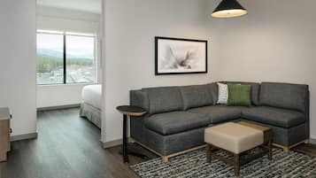 A modern living room with a gray sectional sofa, a small round table, a black pendant light, and a framed abstract artwork.