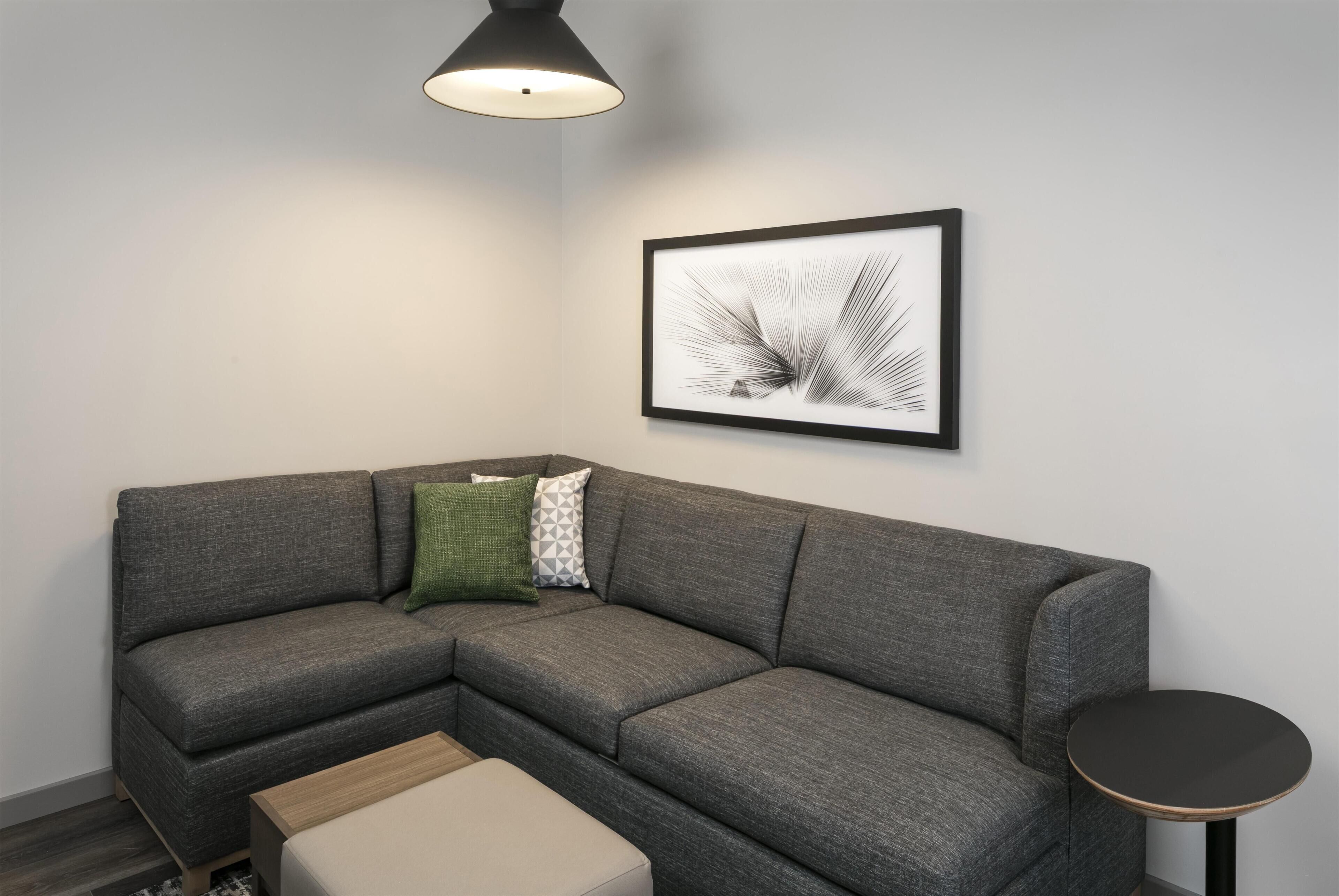 A modern living room with a sectional sofa, a small round table, and a framed abstract artwork on the wall.