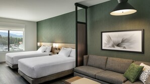 Et hotelværelse med to senge, en sofa, et lille bord og et stort vindue med udsigt til det fri.