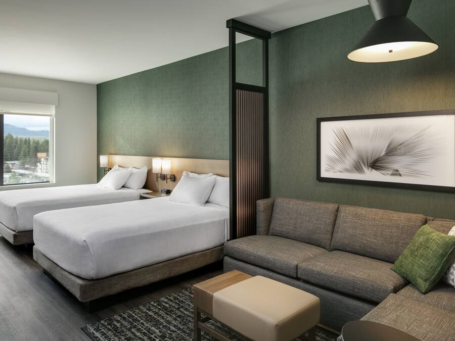Habitación de hotel con dos camas, un sofá, una mesita y un ventanal que ofrece vistas al exterior.