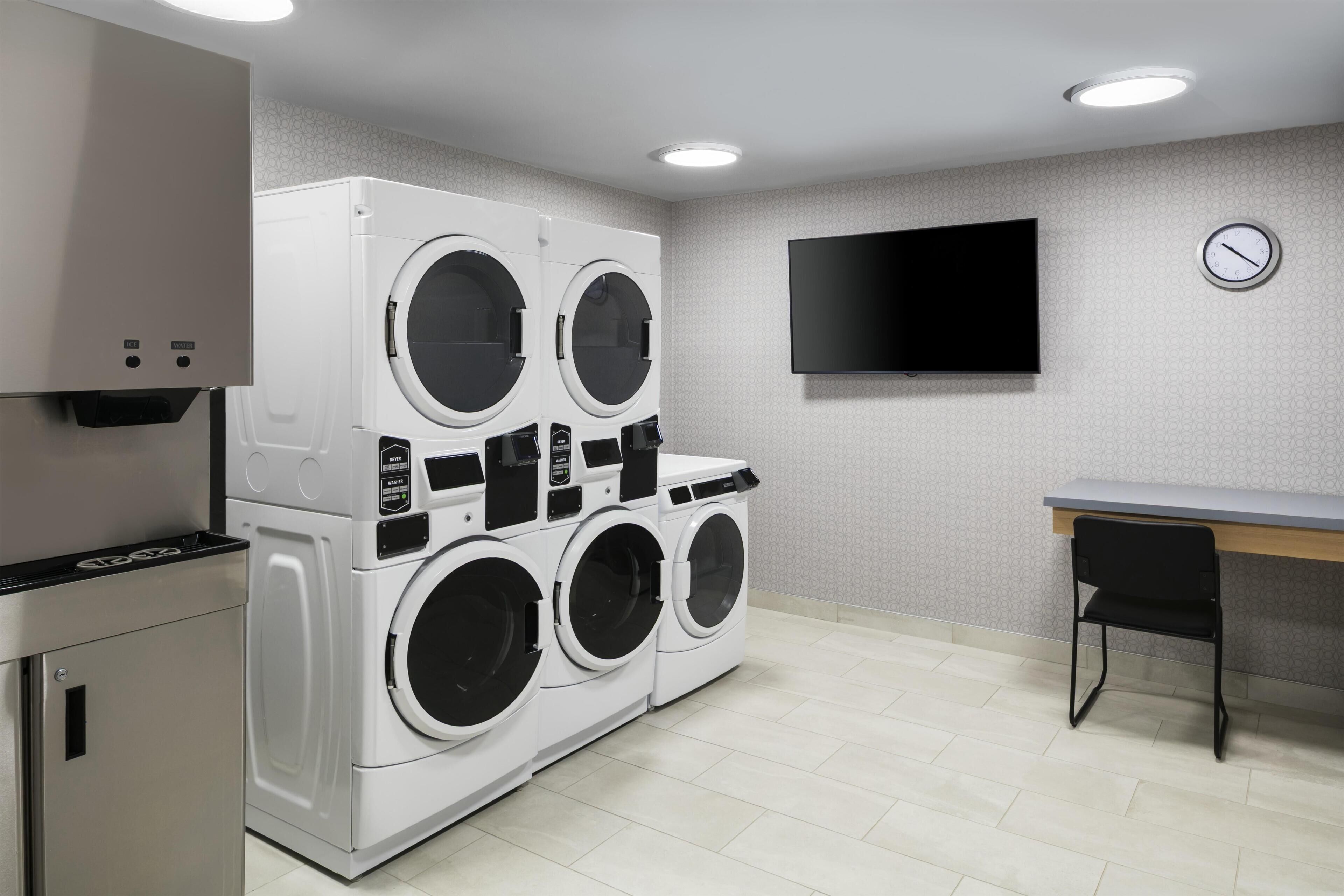 A laundry room with stacked washers and dryers, a flat-screen TV, and a small table.