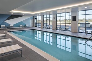 A modern indoor swimming pool with clear glass walls, seating areas, and a view of the parking lot. - Hyatt Place Post Falls/Coeur D'Alene (Post Falls)