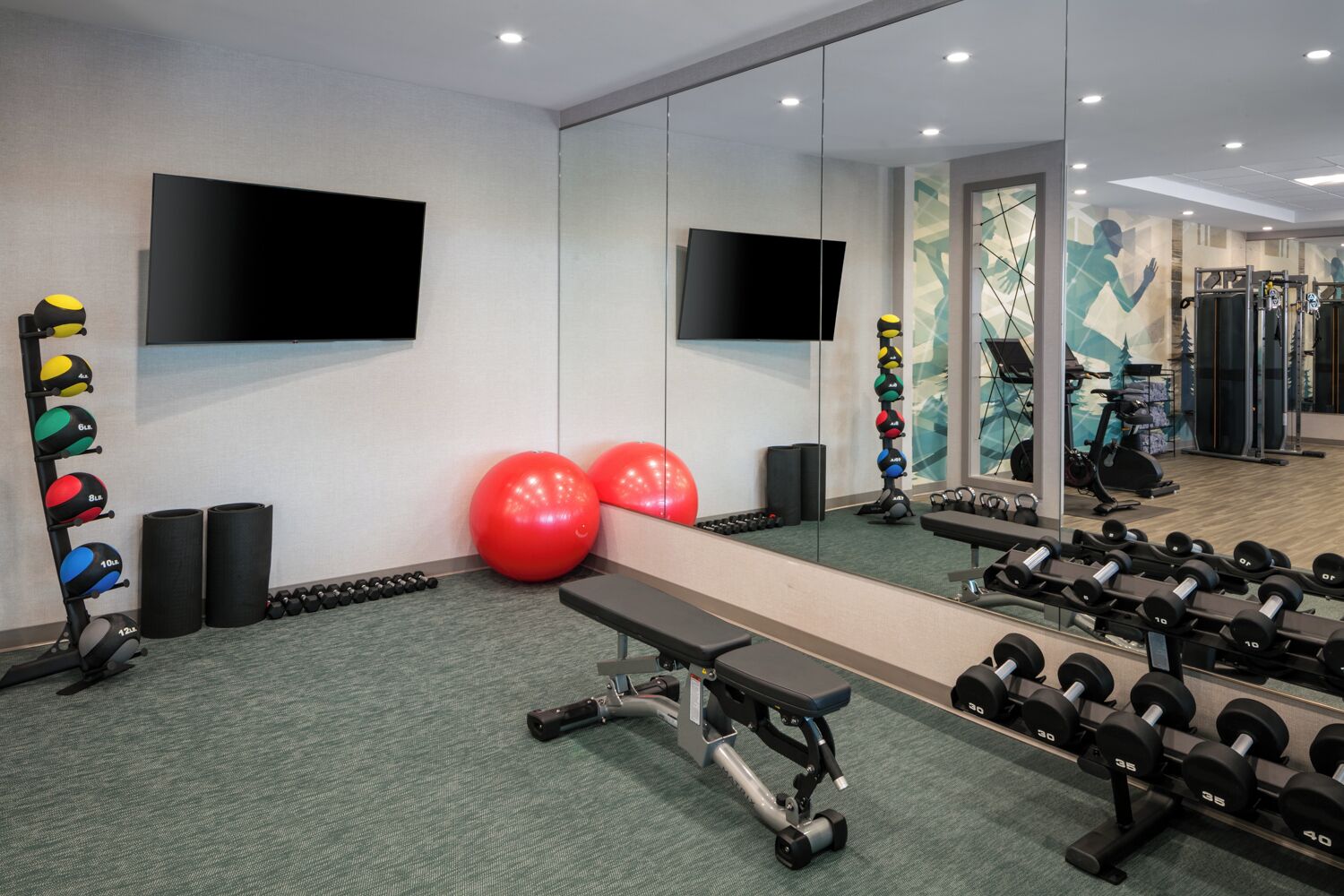 A gym with exercise equipment, a bench, and a large mirror.