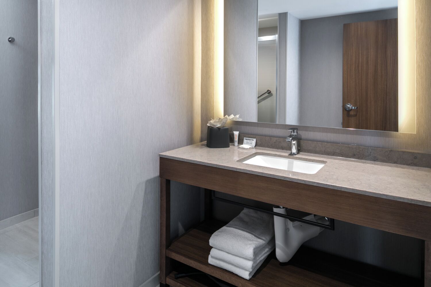 A modern bathroom with a large mirror, a sink, and a towel rack.