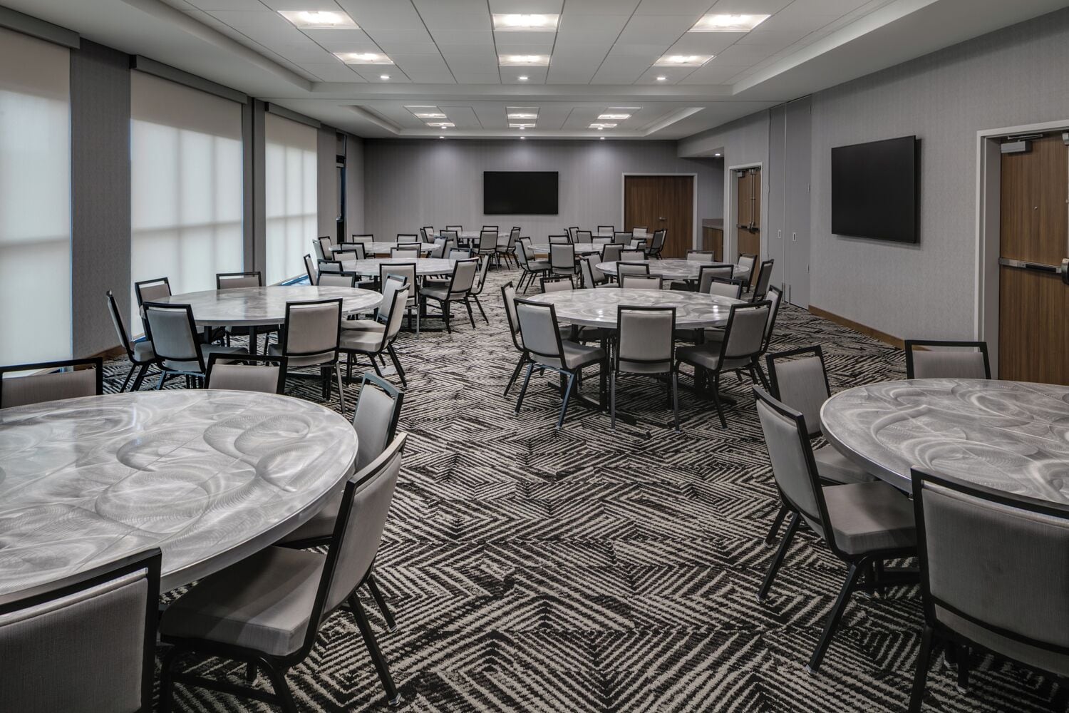 A conference room with multiple round tables and chairs, a patterned carpet, and a large screen on the wall.