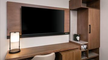 Una habitación de hotel moderna con una televisión de pantalla plana montada en la pared, un escritorio con lámpara, una silla y armarios empotrados.