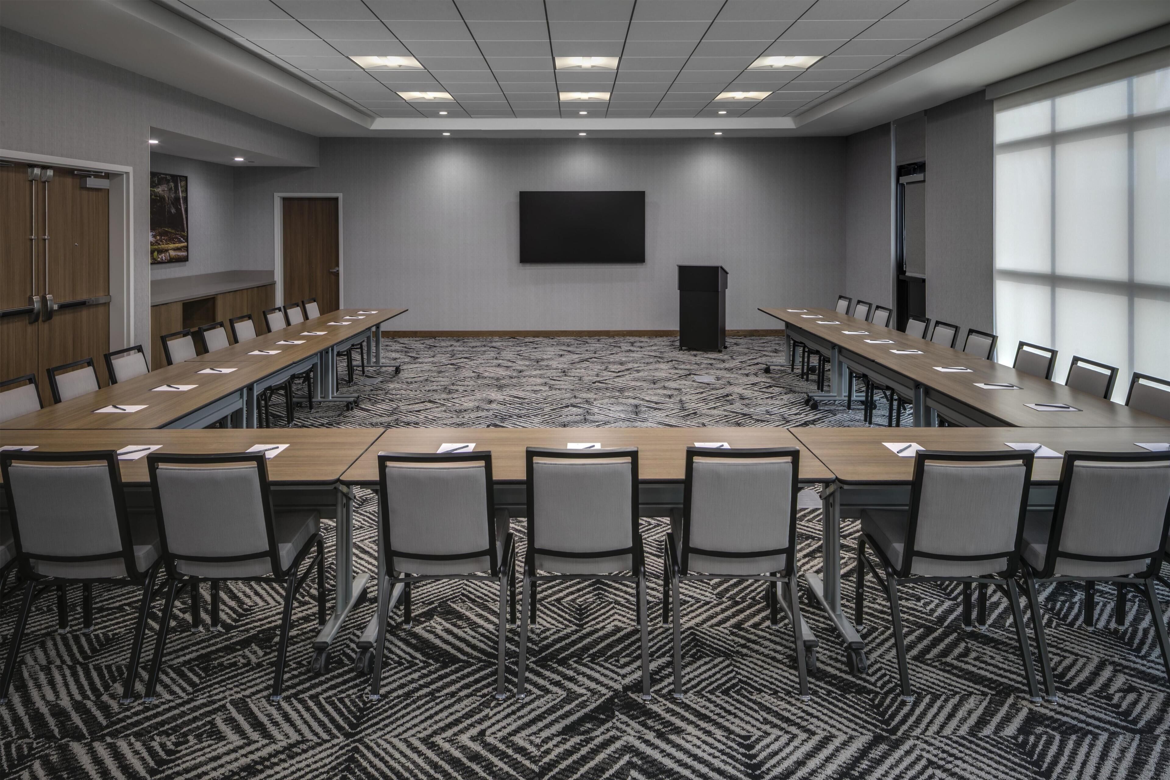 A conference room with a long table, chairs, a podium, and a large screen on the wall.