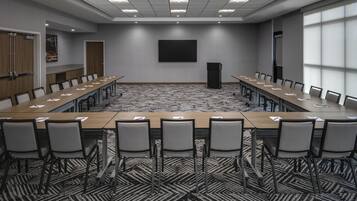Un salón de conferencias con una larga mesa, sillas, un atril y una pantalla grande en la pared.