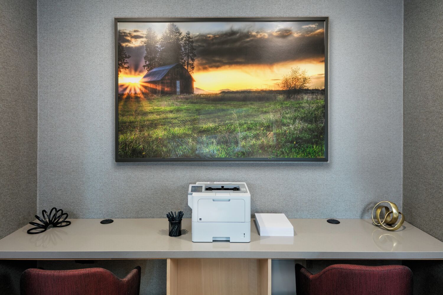 A desk with a printer, a framed landscape photo, and a decorative object on the wall.