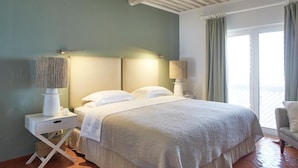 A bedroom with a bed, two bedside tables with lamps, a chair, and a large window with curtains.