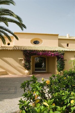 A building with a beige facade, a tiled roof, and a central entrance with a decorative arch. - Vila Joya (Albufeira)
