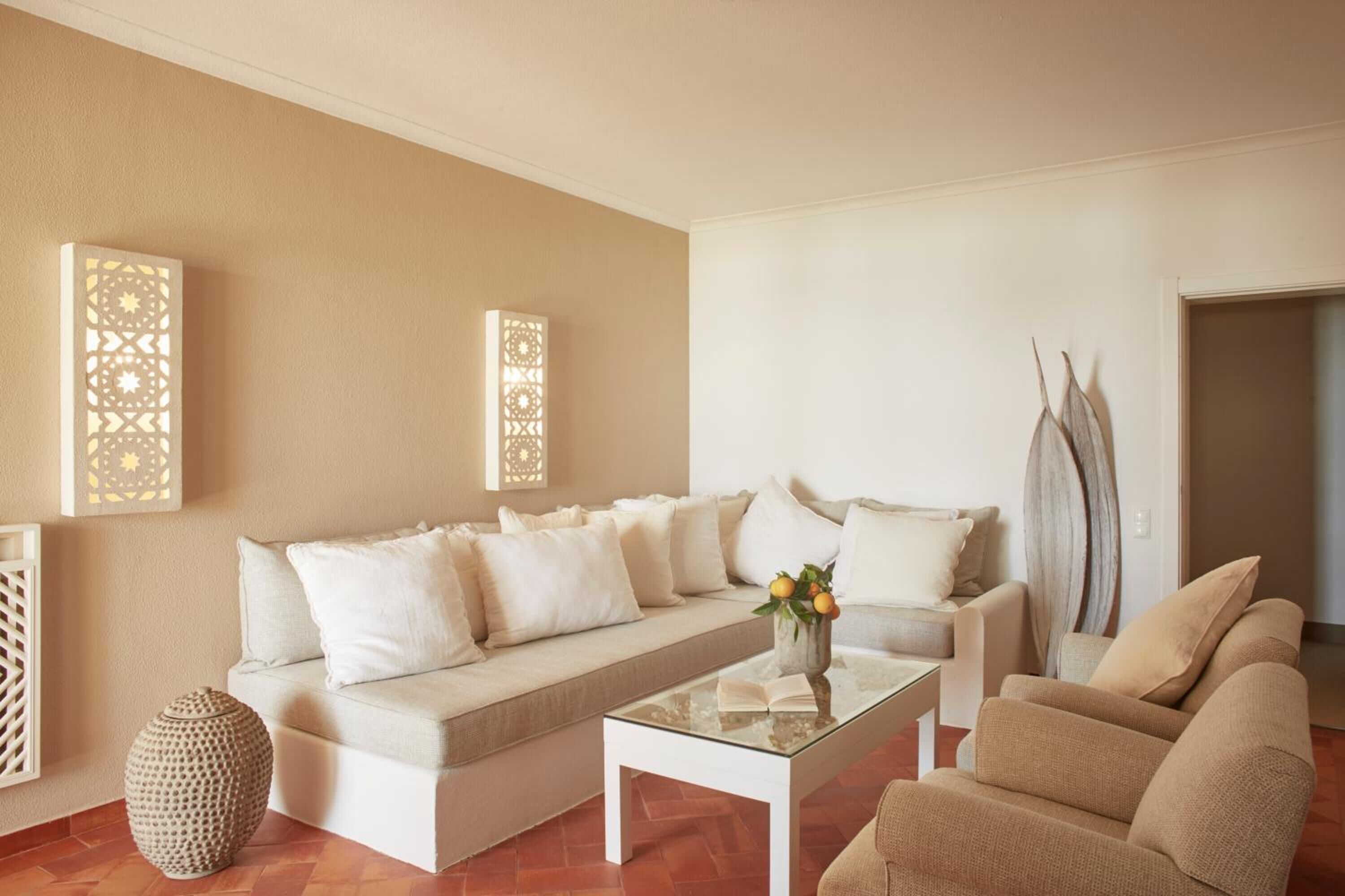 A living room with a beige sofa, a glass coffee table, and a decorative vase with flowers.