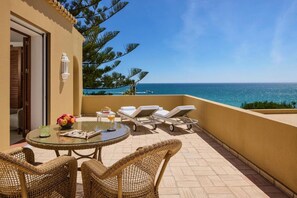 A balcony with a round glass table, wicker chairs, and lounge chairs facing the sea. - Vila Joya (Albufeira)