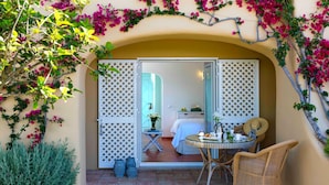 A room with a bed, a small table with a chair, and a view through a door.
