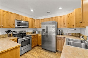 A kitchen with wooden cabinets, stainless steel appliances, a microwave, oven, refrigerator, and a sink.
