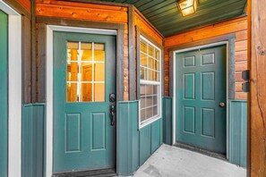 A wooden exterior with two green doors, a small window, and a concrete pathway.