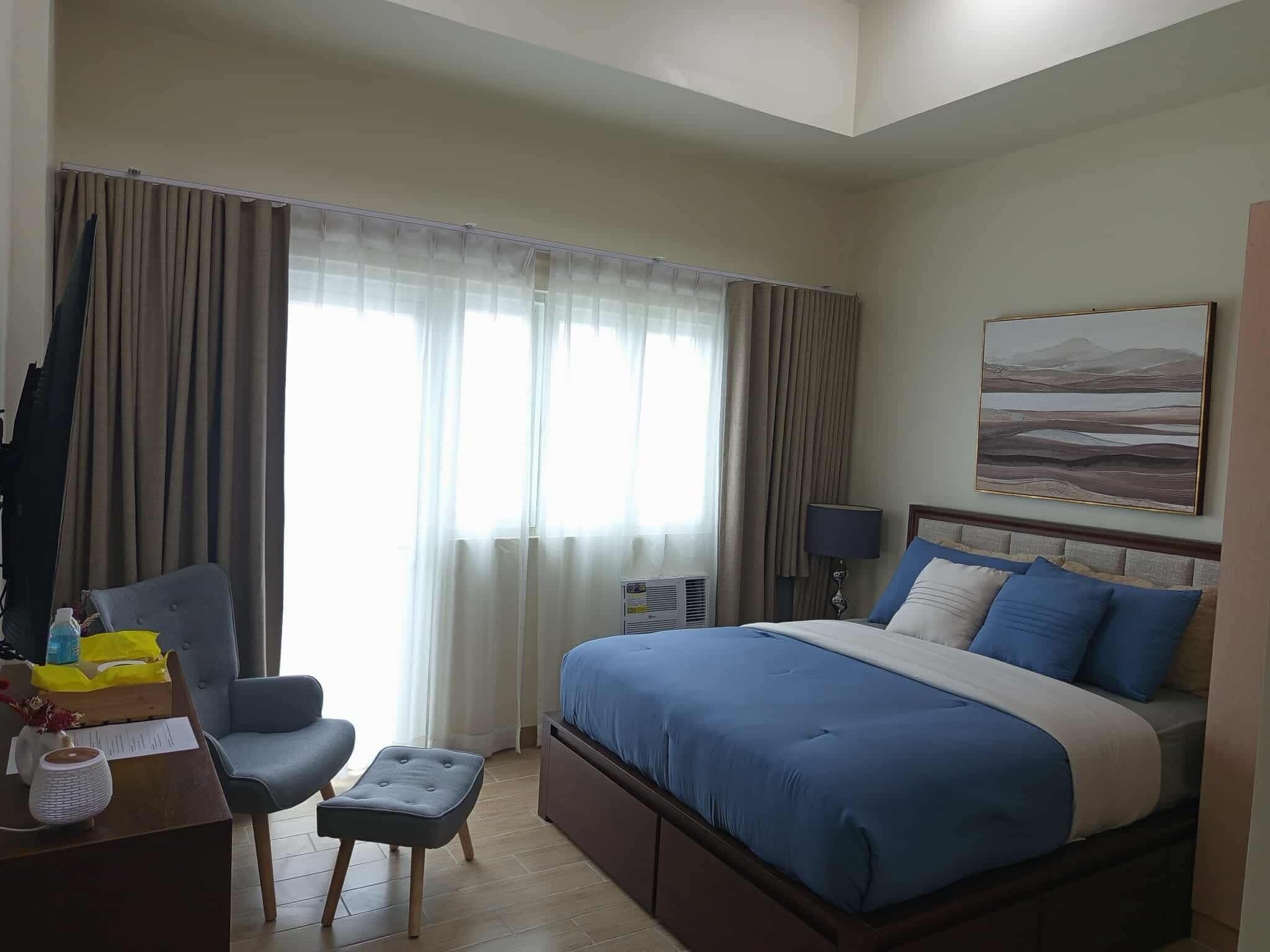 Una camera d'albergo con un letto, una scrivania, una sedia e una finestra con tende.