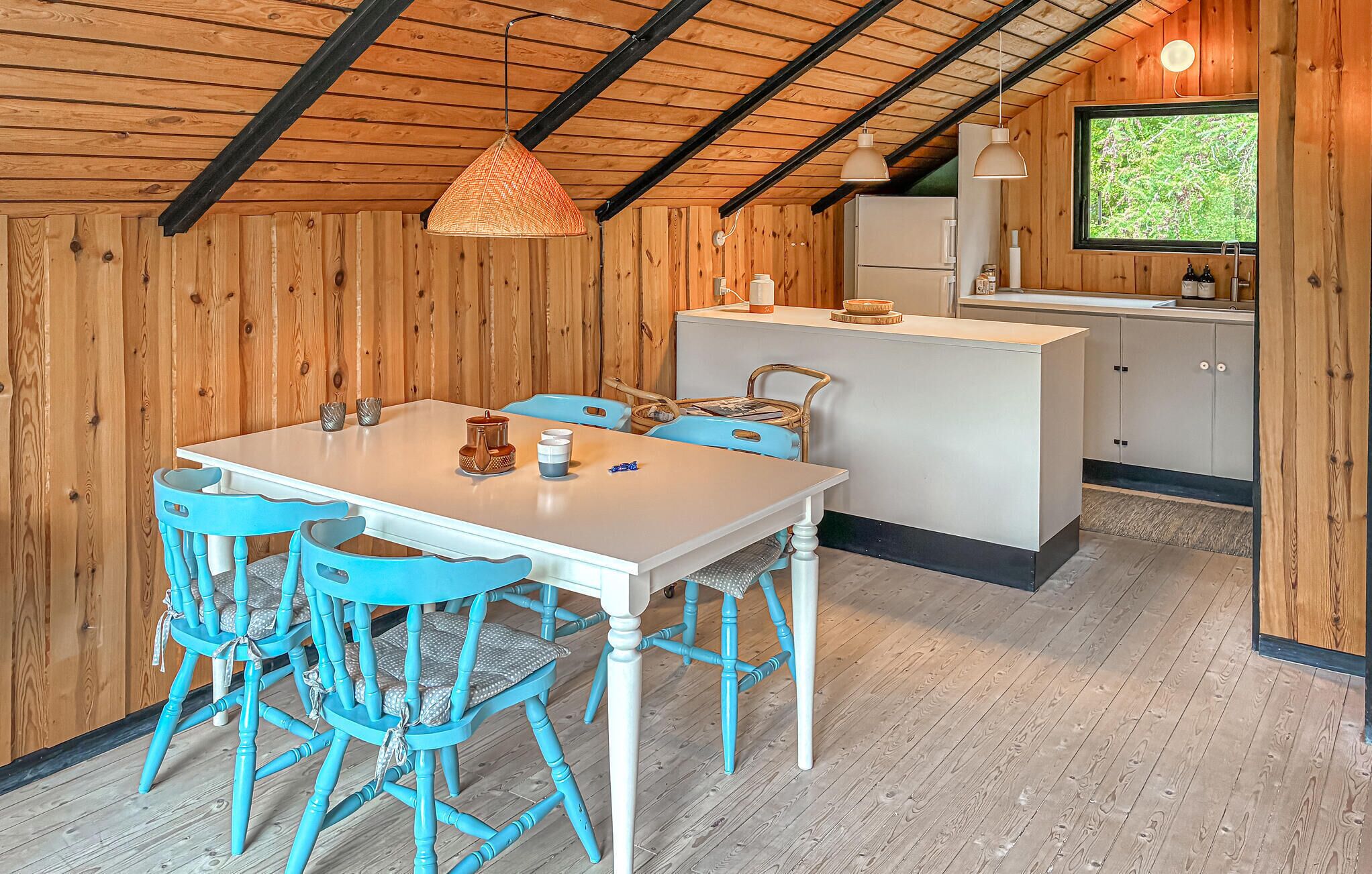 Un intérieur en bois comprenant une table et des chaises, un coin cuisine et une fenêtre donnant sur un paysage agréable.