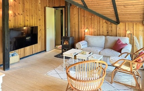 A cozy room with a television, a sofa, two wicker chairs, a small table, and a wood-burning stove.