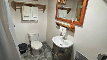 A bathroom with a toilet, sink, and a mirror. There are towels hanging on a rack above the toilet.