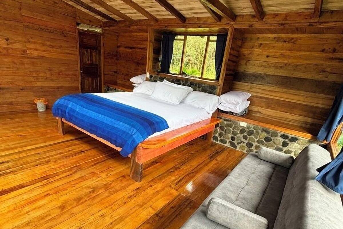 Un dormitorio de cabaña de madera con una cama, un sofá gris y una pared de acento de piedra.