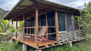 Una cabaña de madera con porche cubierto y amplias ventanas, rodeada de follaje.
