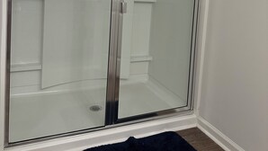 A walk-in shower with a glass door, a white tiled shower area, and a small black rug on the floor. - Room with private bathroom for rent for long periods. (Pooler)
