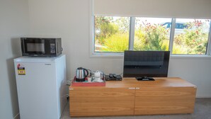 Una kitchenette compacta con microondas, un refrigerador pequeño, cafetera y un televisor de pantalla plana sobre un mueble de madera.